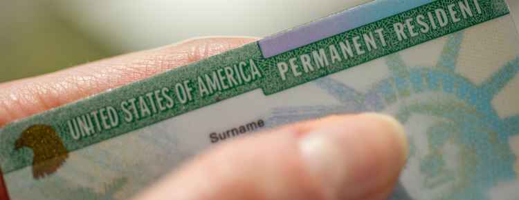 A US citizen holding a US flag and a green card